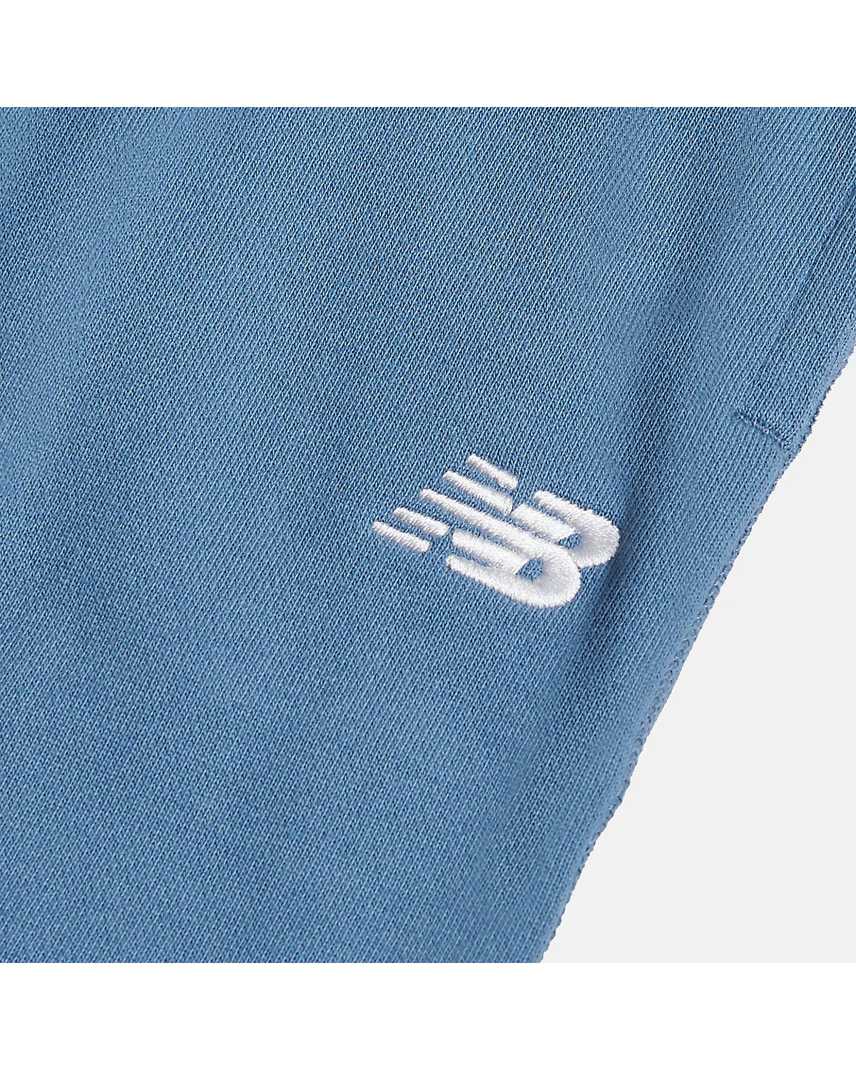 Крупный план белого логотипа New Balance на голубых джоггерах