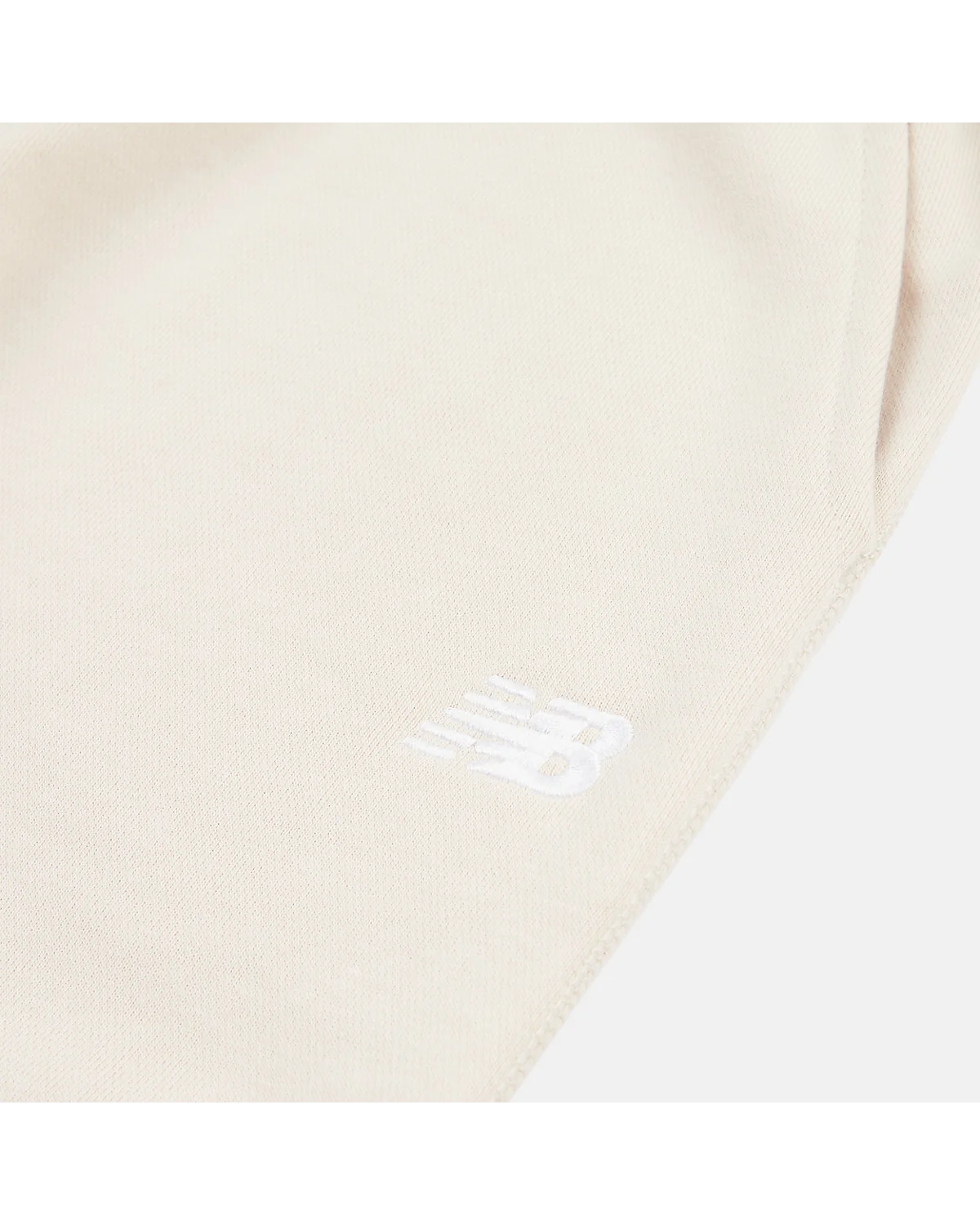 Крупный план вышитого логотипа New Balance на бежевых джоггерах