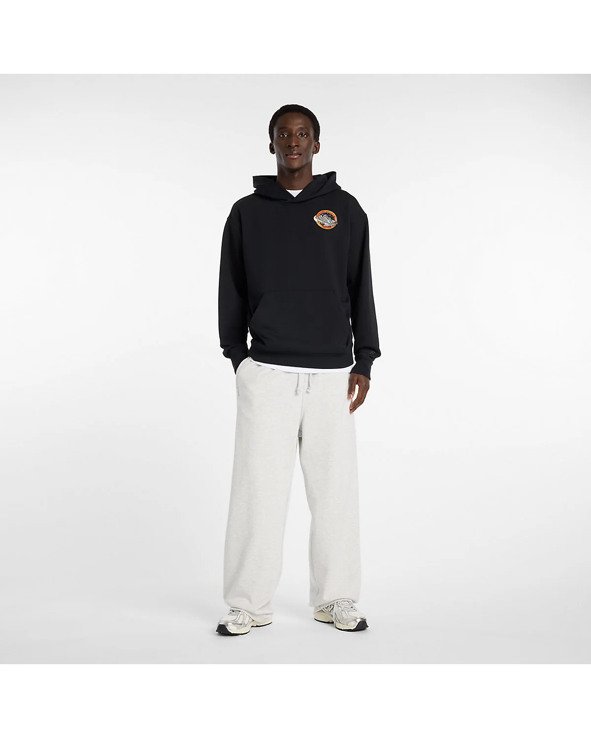 Мужчина в чёрном худи New Balance, полный вид фигуры со светлыми брюками