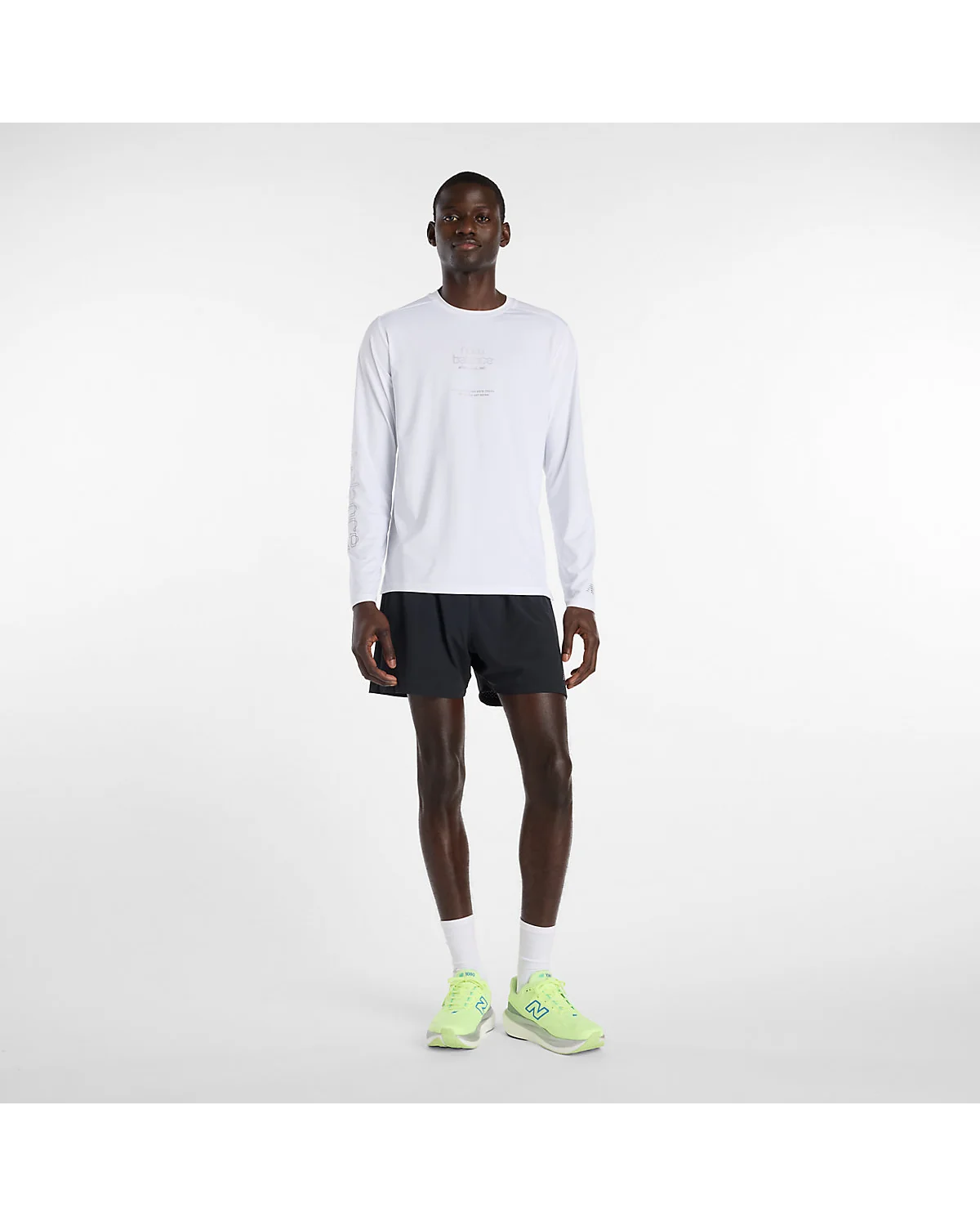 Белый лонгслив New Balance на модели со спортивными шортами и яркими кроссовками, вид сбоку