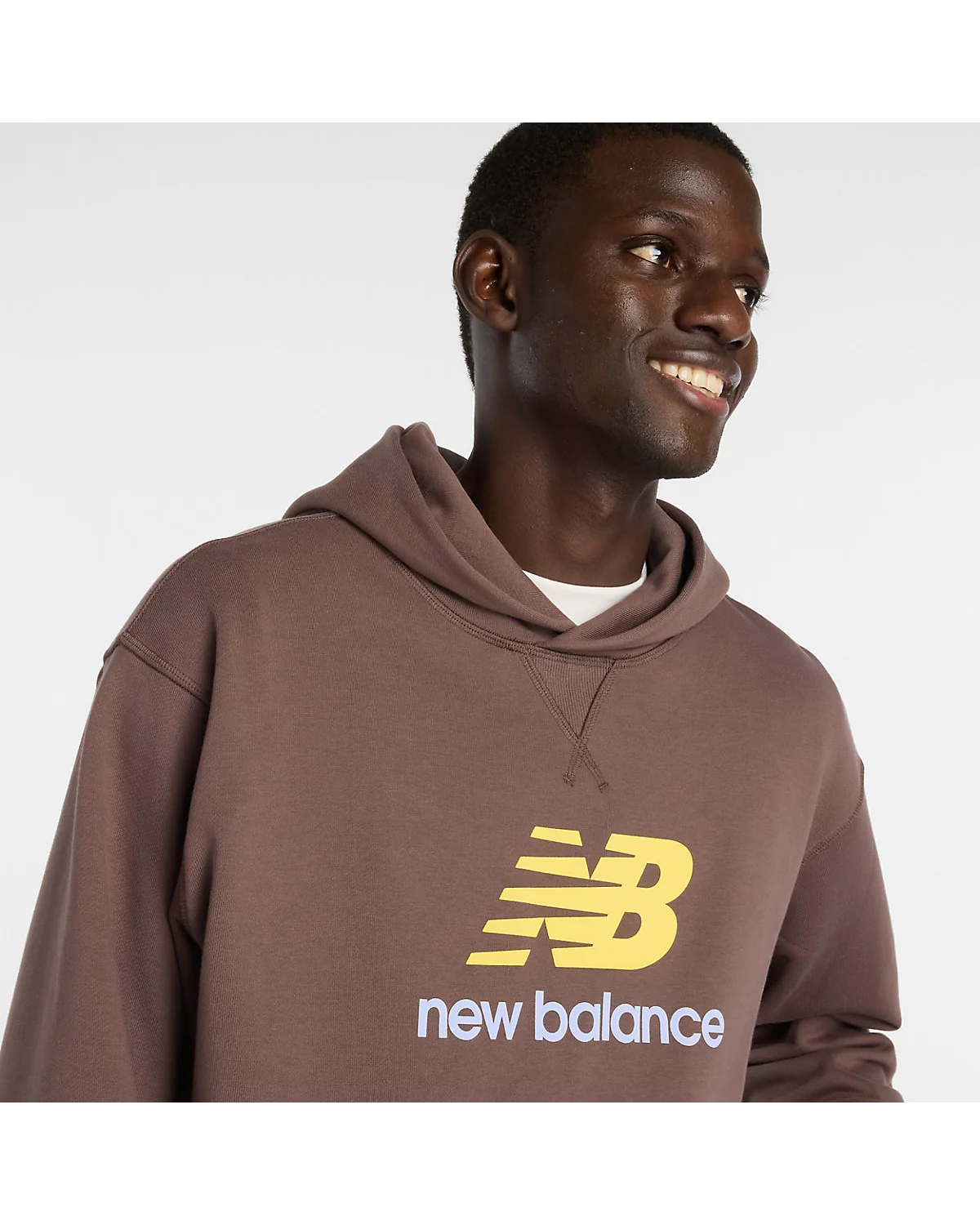 Деталь жёлтого логотипа New Balance на коричневом трикотаже худи