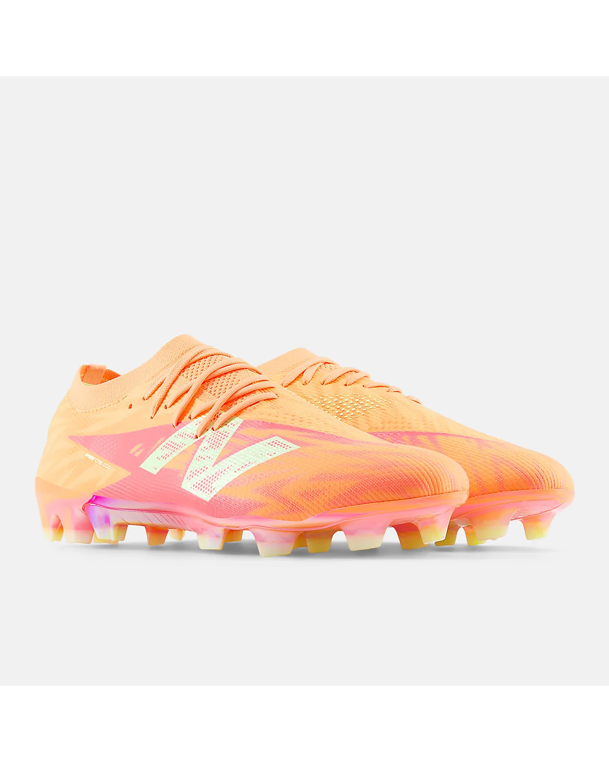 Бутсы New Balance Furon Elite FG V8 цвета манго, ракурс с видимыми шипами FG.