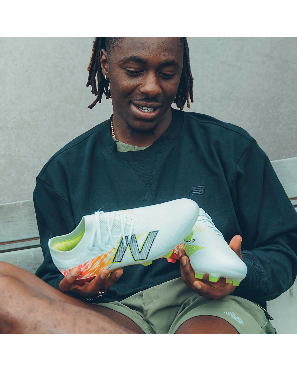 Футбольные бутсы New Balance Furon Elite в руках модели, видны красно-зелёные детали.
