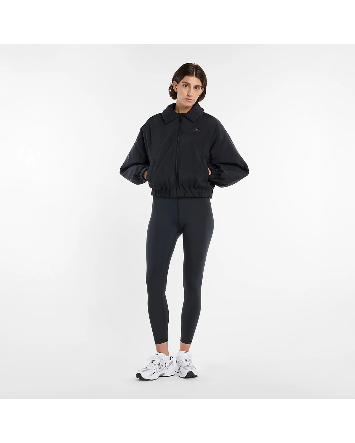 Модель в чёрной куртке-бомбере New Balance и чёрных брюках, полный вид.