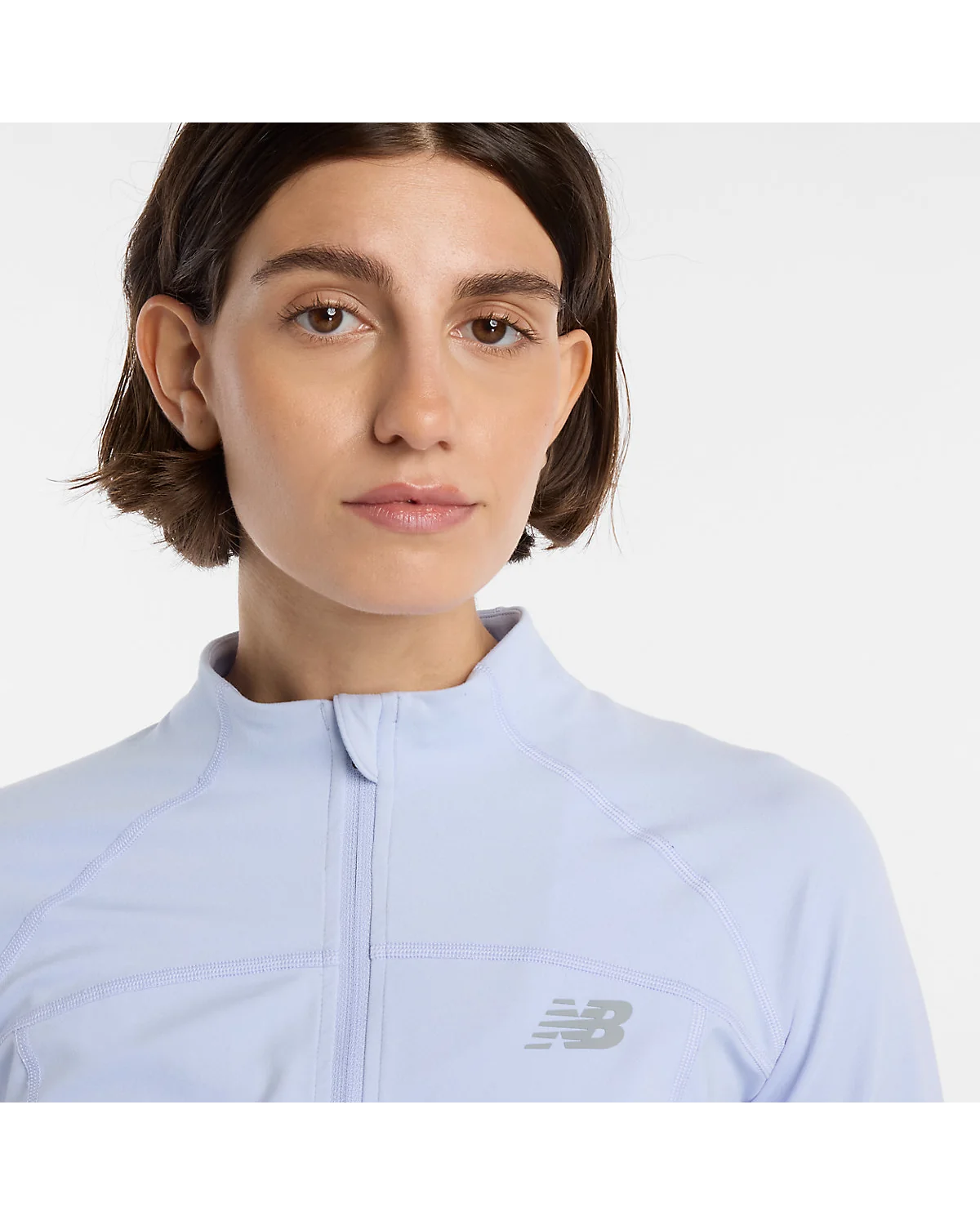 Модель в голубой куртке New Balance Harmony и светлых брюках, полный вид.