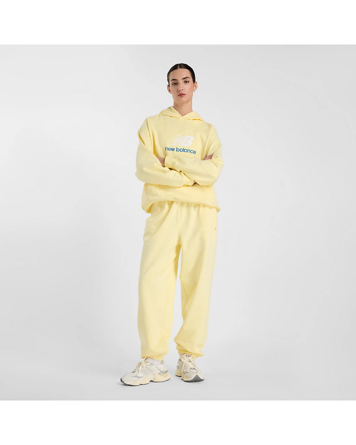 Деталь логотипа на груди жёлтой толстовки New Balance Athletics.