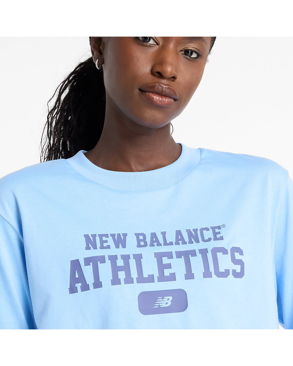 Деталь фиолетового логотипа на груди голубой футболки New Balance.