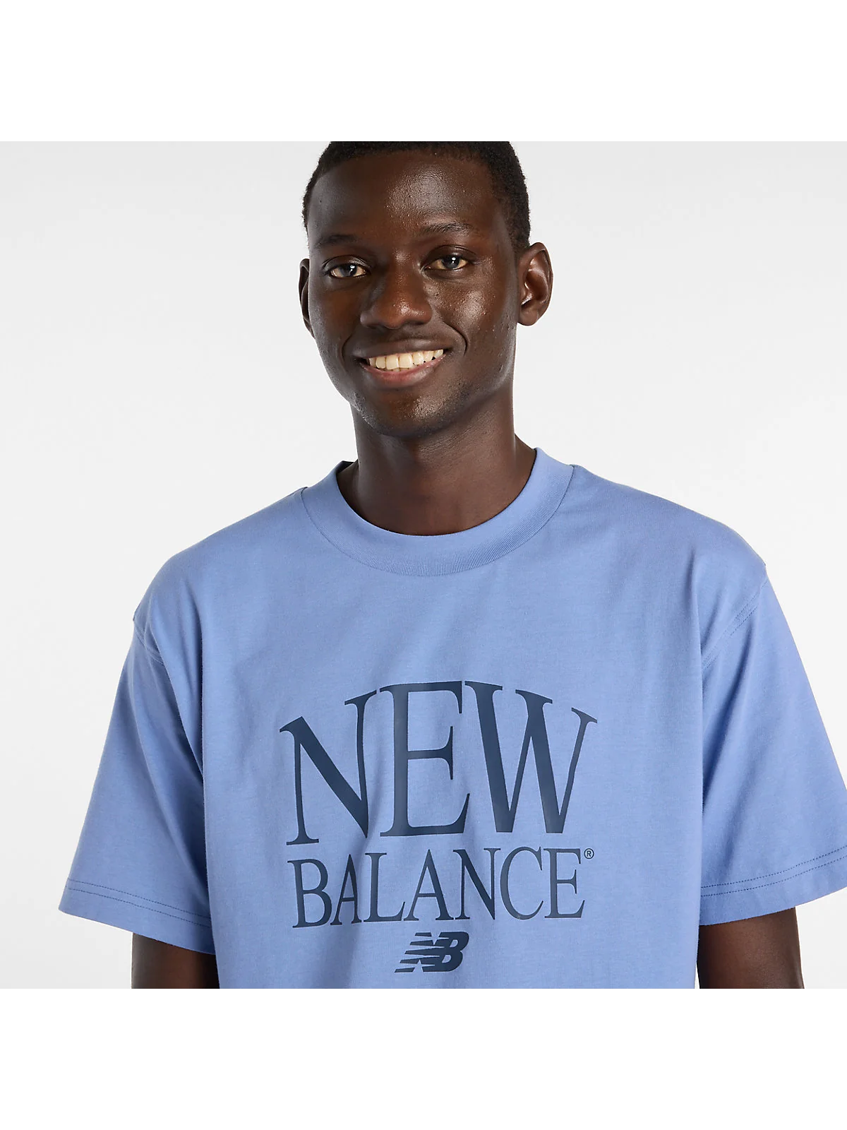 Крупный план белого фирменного принта New Balance на чёрной ткани футболки