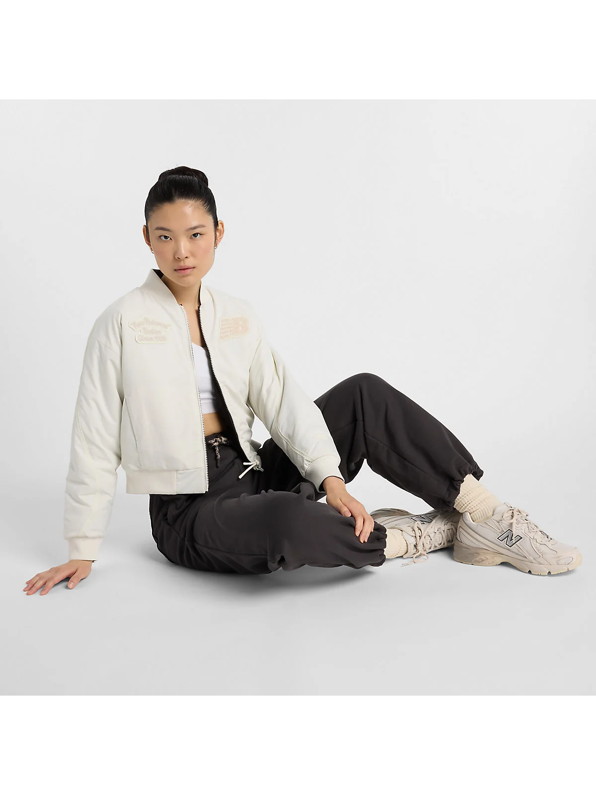 Бежевые брюки New Balance на модели в тёмном верхе, в интерьере.
